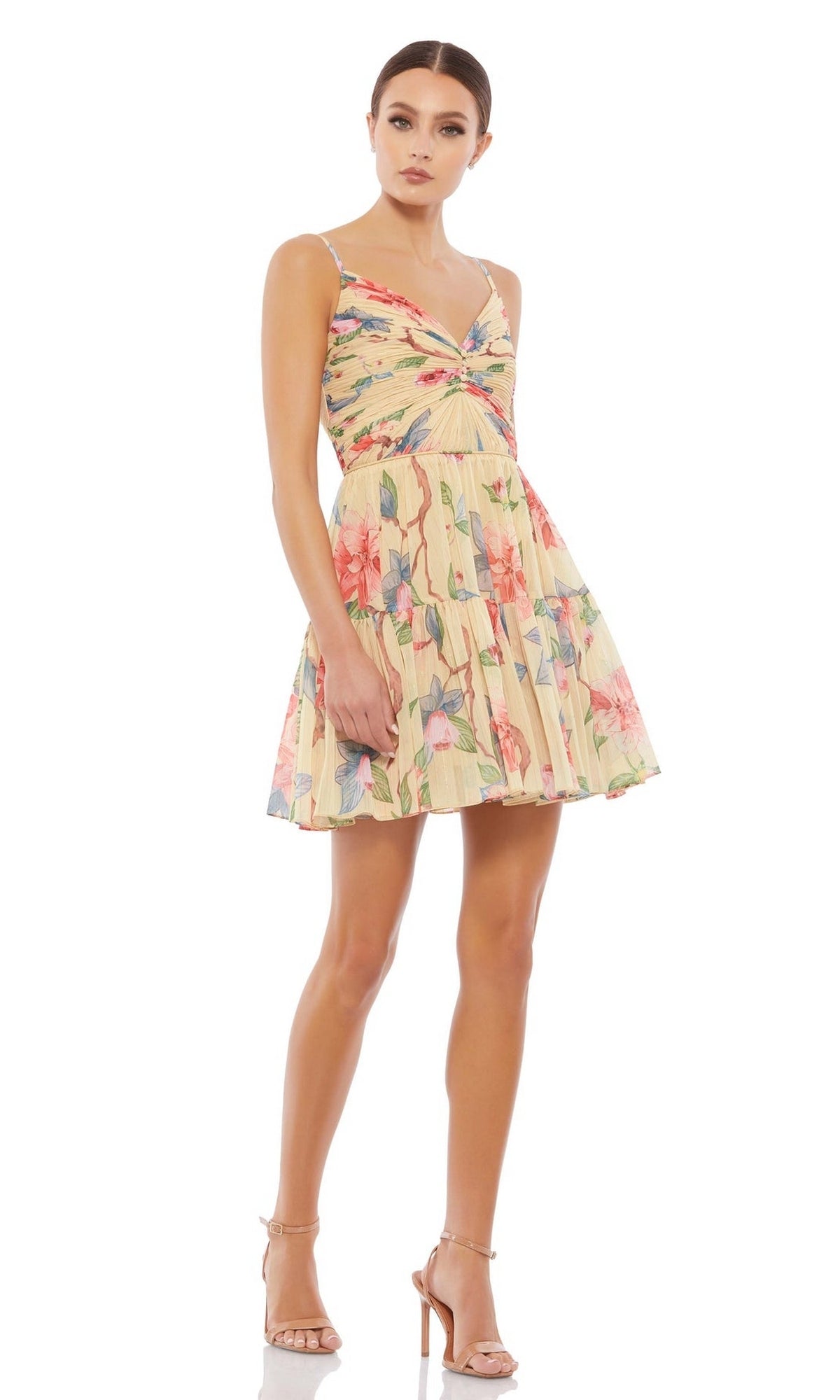 A woman in the Short Wedding Guest Dress 70204 by Mac Duggal—yellow, floral print, sleeveless with a v-neckline and pleated skirt—paired with nude high-heeled sandals.